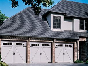 Three white garage doors on a large home with dark gray roof.