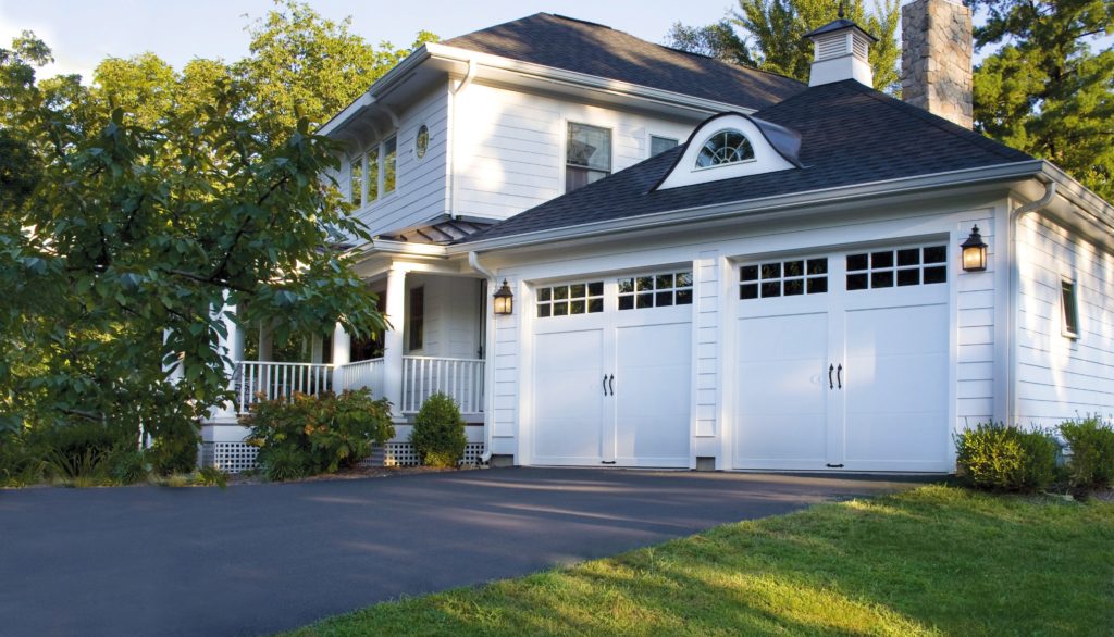 Two white Clopay Coachman garage doors on large two-story white home with trees surrounding.