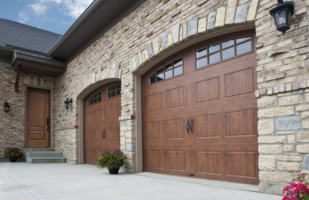 Two woodgrain arch-topped Clopay garage doors in a stone home.