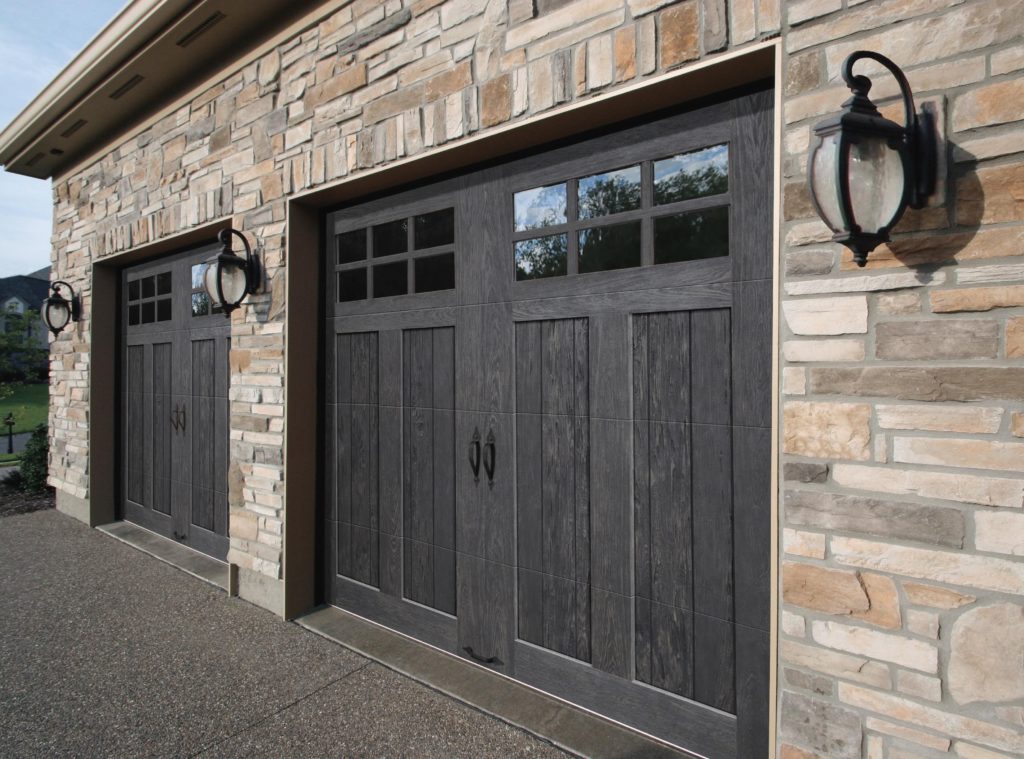 Two black Clopay Canyon Ridge garage doors on a light stone garage