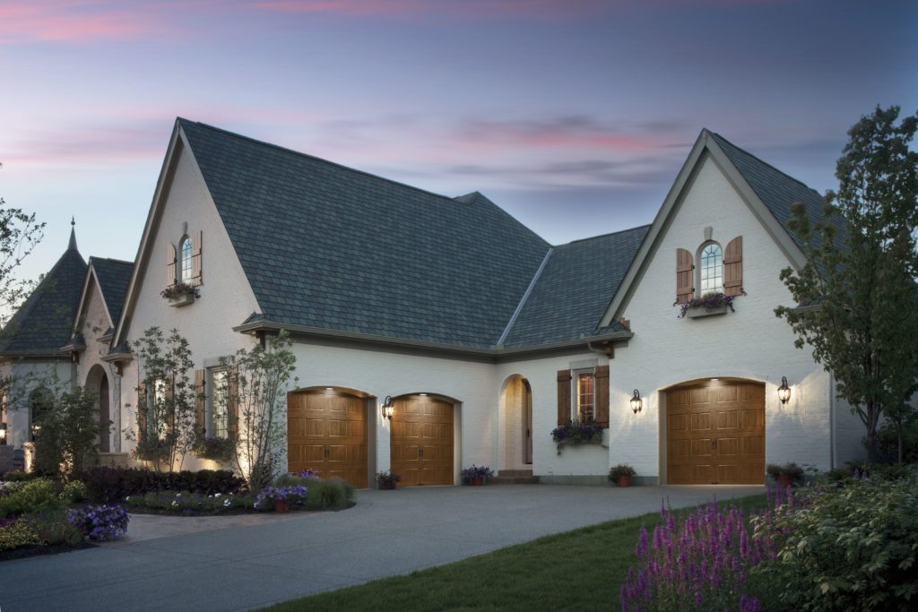 Clopay Ultra Grain windowless garage doors: Three woodgrain garage doors in a large white stucco home with A-frame roof, at sunset.